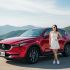 2026 Mazda CX-5 in red parked at a scenic mountain viewpoint with a young Asian woman in a white dress standing beside it