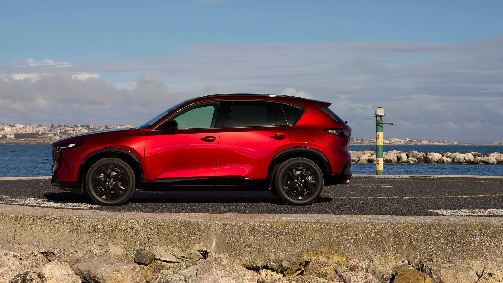 Side view of the 2026 Mazda CX-5 in red, elegantly parked at a scenic pier.