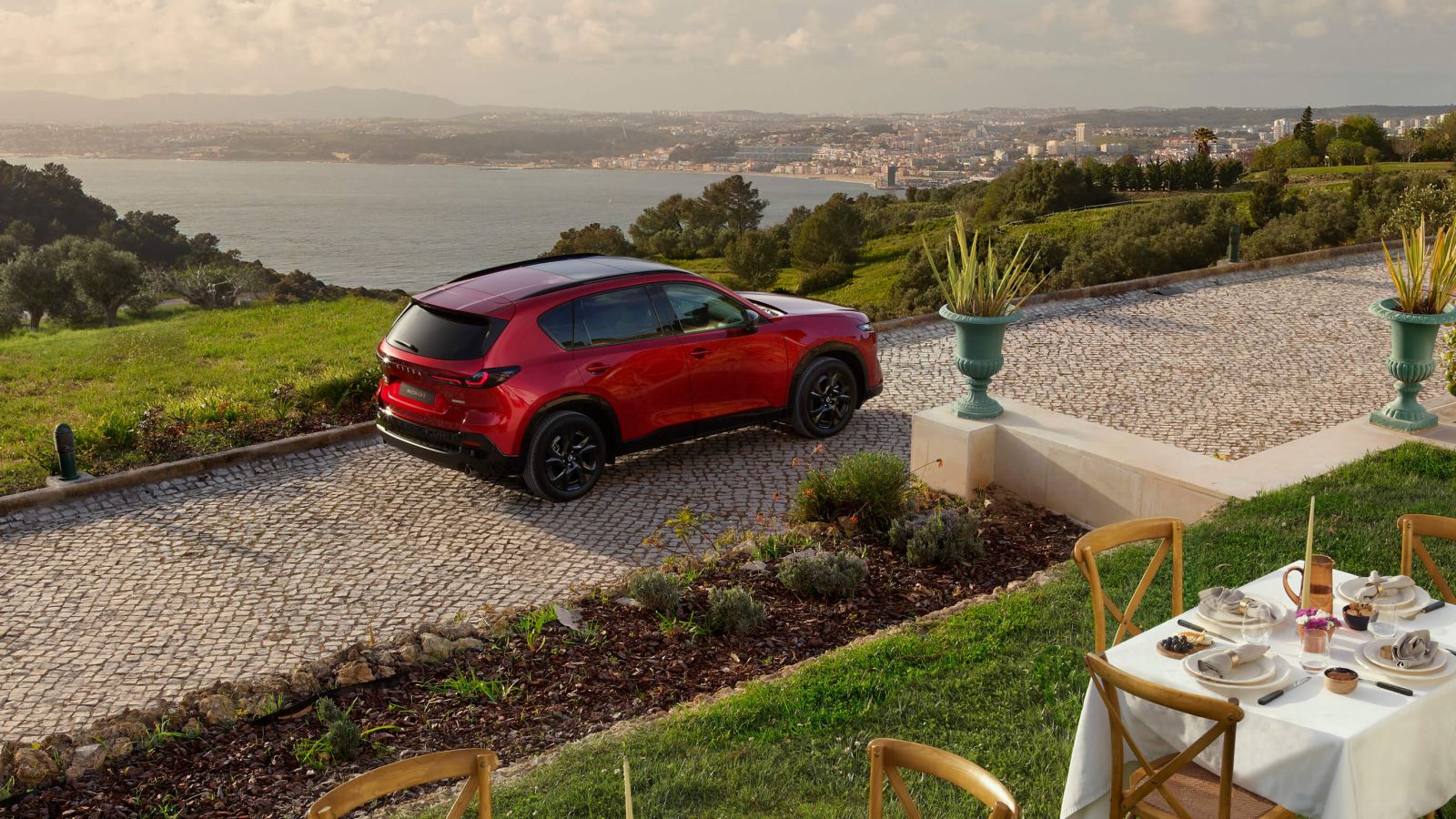 Drone shot of the 2026 Mazda CX-5 from the rear, parked in a driveway with the ocean in the background