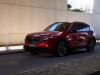 The 2026 Mazda CX-5 driving down a city street, shown from the driver-side angle.